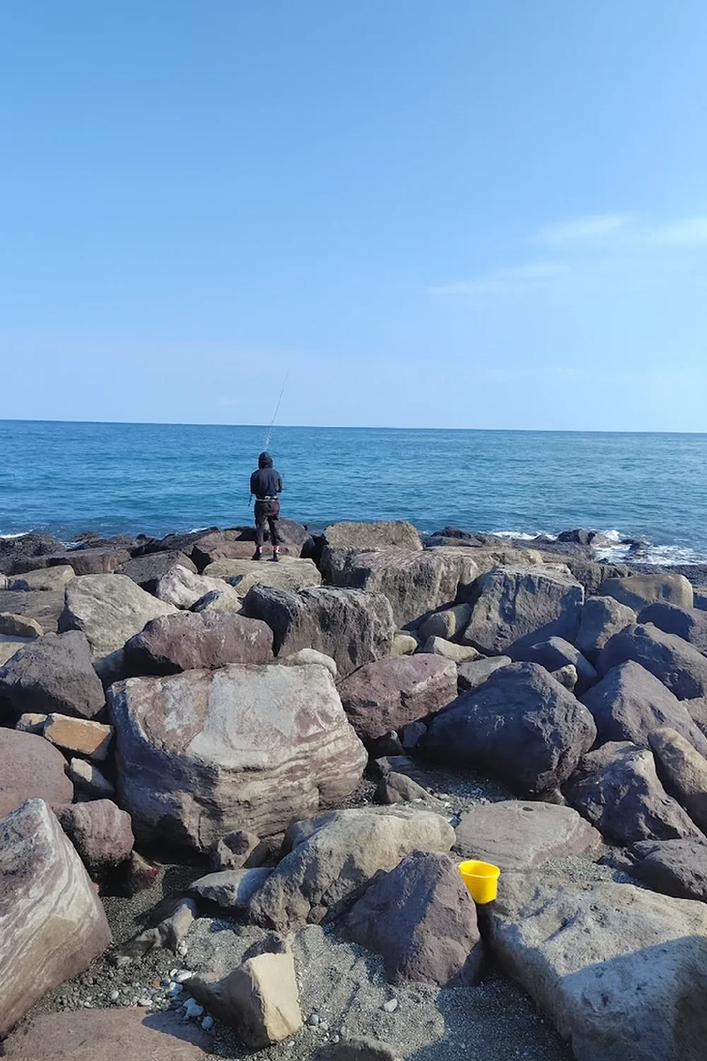 御幸の浜の石積み突堤で釣りをする人